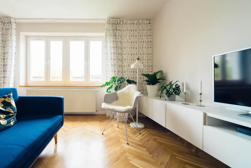 Minimalist living room with blue sofa, wooden floor, indoor plants, and modern white furniture