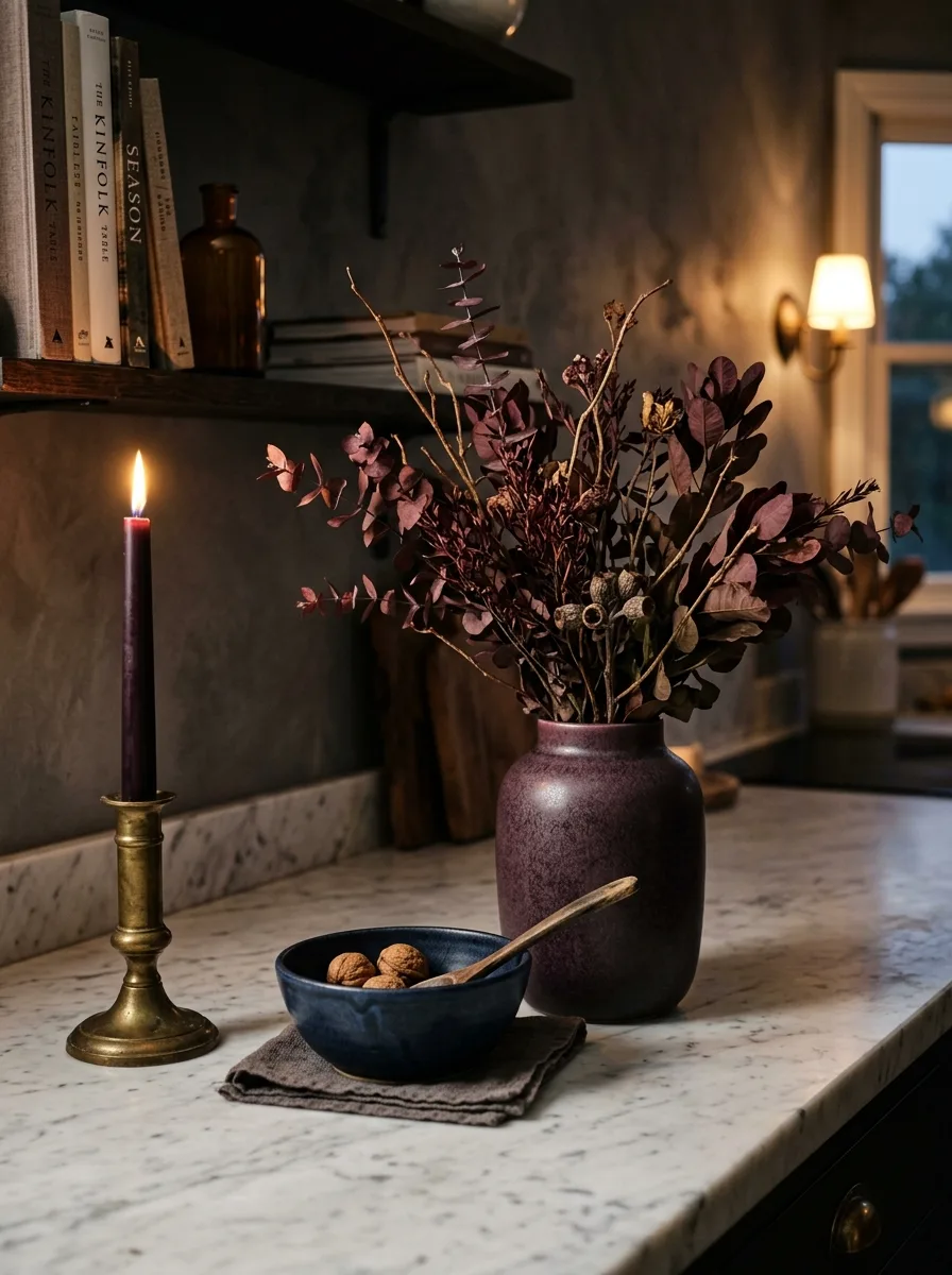 Dark plum ceramic vase with burgundy branches, navy bowl, and eggplant candle on white marble kitchen counter for cozy kitchen decor for fall