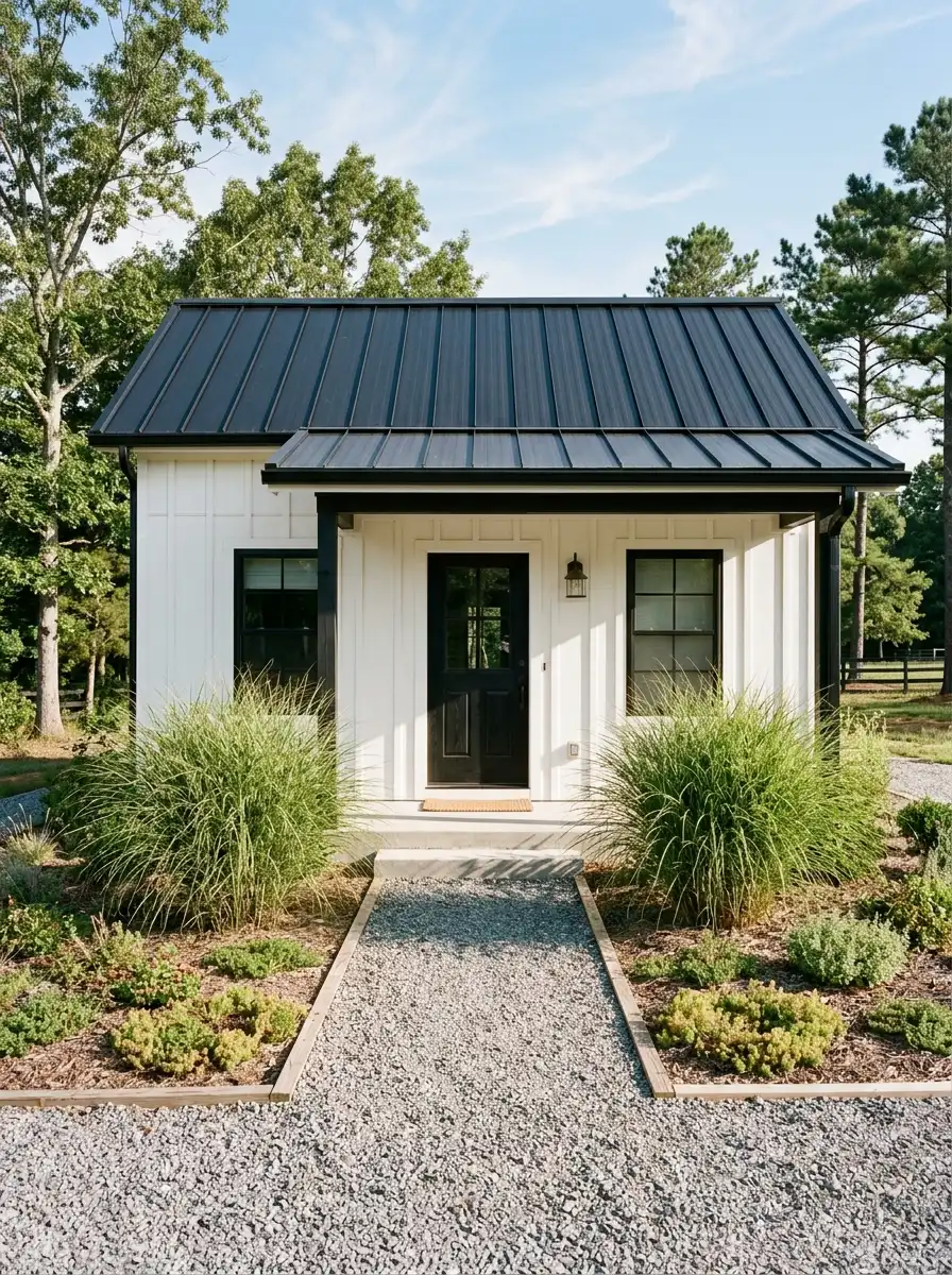 19 Stunning Small Barndominium Exterior Ideas That Prove Simple Barn House Designs Can Make a Big Impact 18 Small barn style home exterior with white vertical siding and black metal roof surrounded by simple gravel path, symmetrical ornamental grasses, and native ground cover