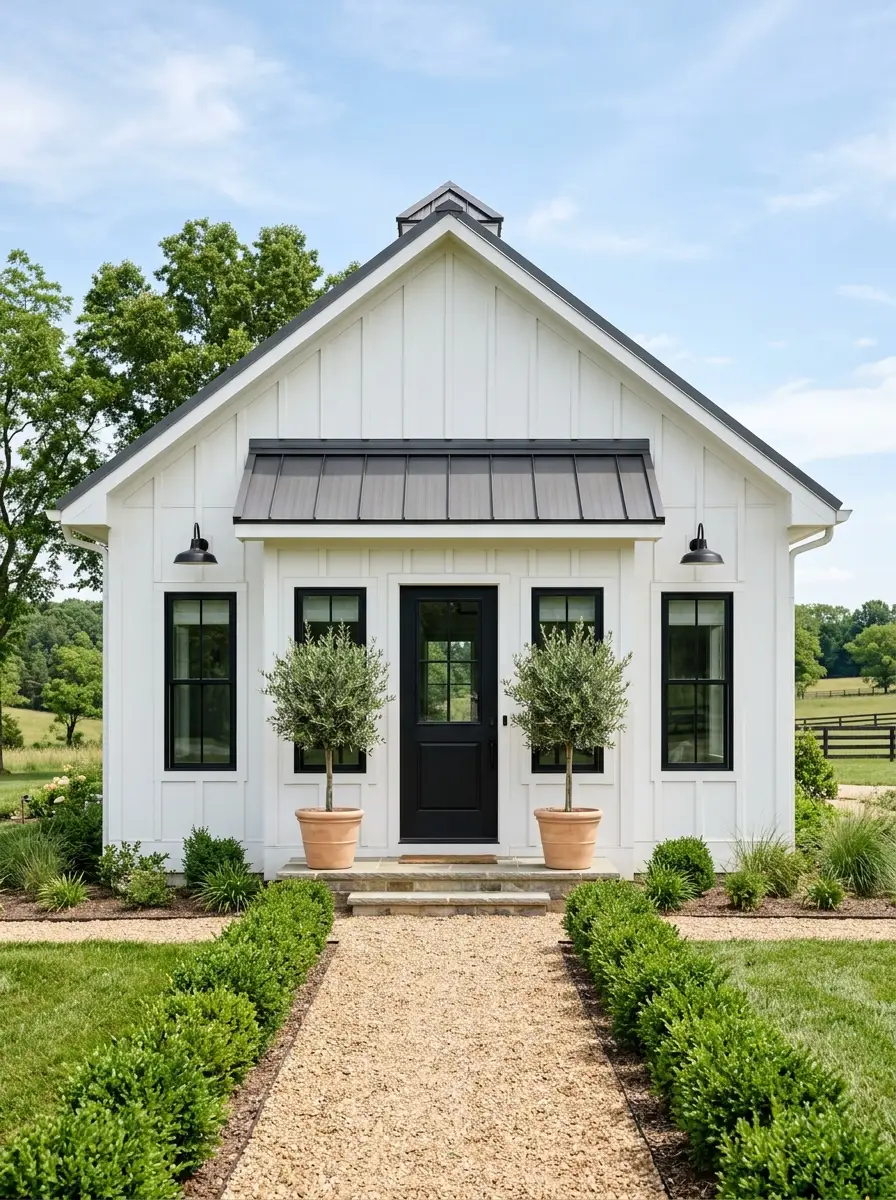 19 Stunning Small Barndominium Exterior Ideas That Prove Simple Barn House Designs Can Make a Big Impact 4 Symmetrical small barndo exterior with white siding, centered black front door, matching windows, and olive trees flanking the entry steps